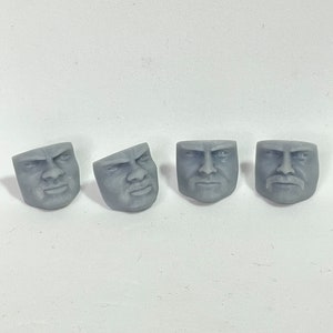 May include: Four grey plastic male heads with different facial expressions. The heads are all the same size and shape, but have different expressions, including a neutral expression, a surprised expression, a frowning expression, and a smiling expression.