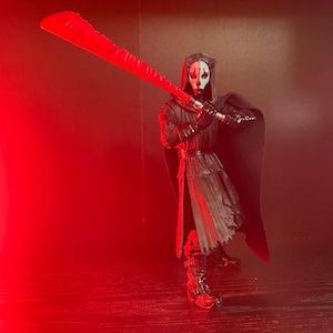 May include: A Star Wars action figure of Darth Nihilus, a Sith Lord, holding a large red lightsaber. The figure is dressed in a black hooded cloak and armor, with a white mask. The background is a dark red.