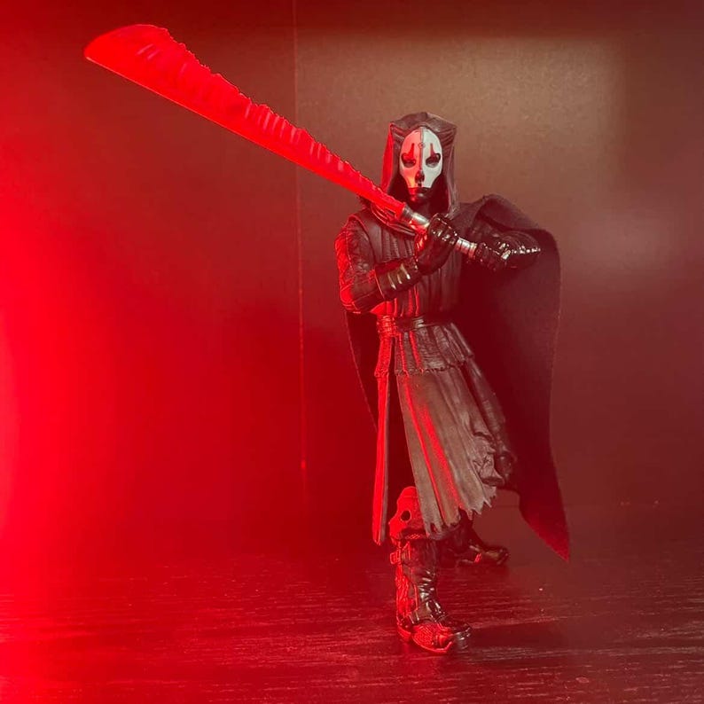 May include: A Star Wars action figure of Darth Nihilus, a Sith Lord, holding a large red lightsaber. The figure is dressed in a black hooded cloak and armor, with a white mask. The background is a dark red.