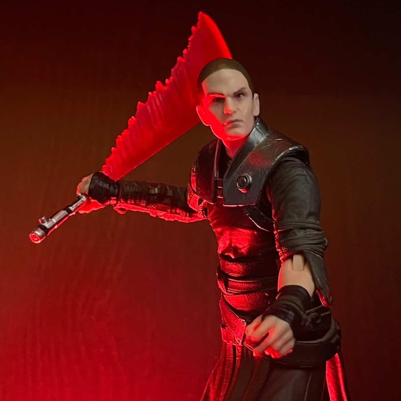 May include: A figure of a character from a science fiction franchise, holding a red lightsaber. The figure is dressed in a black outfit with a silver and black hilt. The background is a dark red.