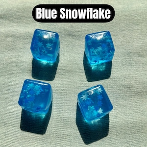 May include: Four translucent blue cubes with snowflake inclusions. The cubes are arranged on a light green surface. The text "Blue Snowflake" is displayed in a black oval above the cubes.