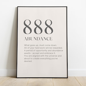 May include: A framed print with the number 888 and the word "ABUNDANCE" in a dark gray font. The print includes text about hard work and opportunity. The frame is black, and the background is a light beige color.