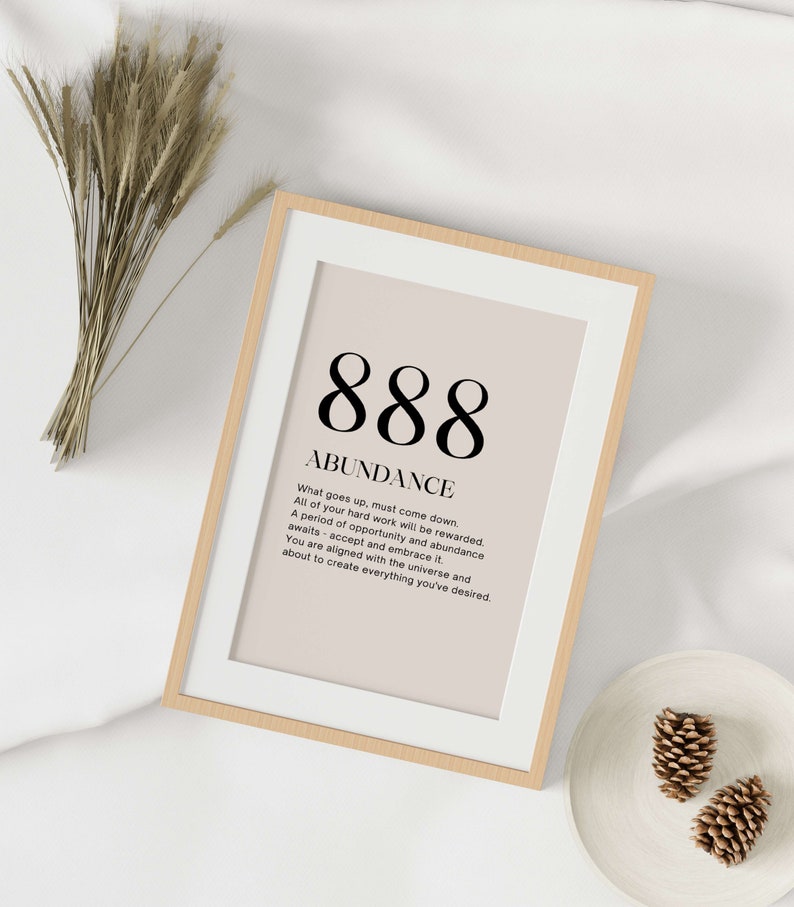 May include: Framed print with the number 888 and the word "ABUNDANCE" in a minimalist design. The print has a beige background and a white border, encased in a light wood frame. The text below describes abundance and opportunity.