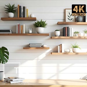 Op de afbeelding: Een reeks horizontale houten zwevende planken gemonteerd op een witte wand van schrootjes. De planken bevatten diverse boeken, groene potplanten, kleine decoratieve objecten en ingelijste kunst. Een grote plant staat op een houten bureau eronder.