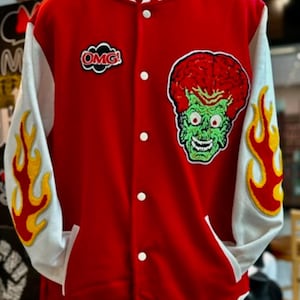 Puede incluir: Chaqueta de béisbol roja y blanca con una cabeza de extraterrestre verde y un parche "OMG!" en la parte delantera. Las mangas tienen llamas amarillas.