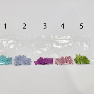 May include: Five small bags of butterfly shaped glitter, each bag is labeled with a number 1 through 5. The glitter is in the following colors: turquoise, lavender, magenta, pink, and green.