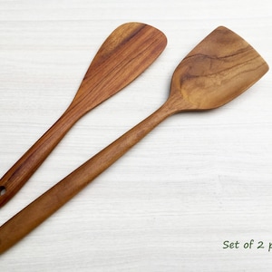 May include: A set of two brown wooden kitchen spatulas with visible grain patterns. Each spatula features a long handle with a circular hole at the end for hanging. The text "Set of 2 pcs." is printed in the lower right corner of the image.