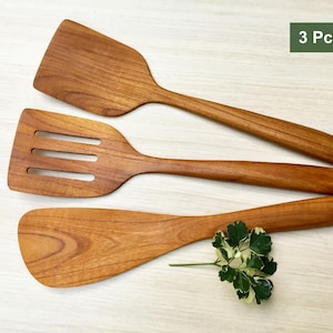 以下が含まれることがあります： 木製のキッチンヘラ3点セット。ヘラは天然木で作られており、滑らかで磨かれた仕上げになっています。セットには、スロット付きヘラ、ソリッドヘラ、フラットヘラが含まれています。ヘラは明るい木製の表面に配置されています。3 Pcs. Set