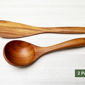 May include: A two-piece set of kitchen utensils made from light brown wood with visible grain patterns. The set includes a flat, wide spatula and a deep, rounded ladle with a small hole at the end of the handle. The text 2 Pcs. Set is visible.