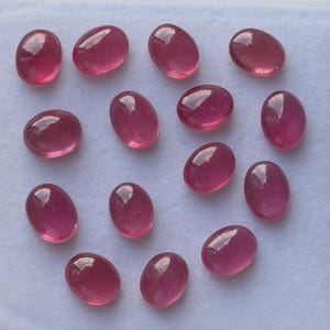 May include: A collection of oval-shaped, polished gemstones in varying shades of pink and red. The gemstones are smooth and translucent, with a glossy finish. The arrangement suggests they are loose stones, possibly for jewelry making or collecting.