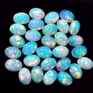 Puede incluir: Un conjunto de ópalos ovalados con una base azul lechoso y destellos iridiscentes de verde, rosa y amarillo. Las piedras preciosas están dispuestas juntas sobre un fondo negro, mostrando su juego de colores único.