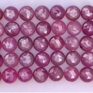 May include: A collection of faceted, round gemstones in varying shades of pink and magenta. The gemstones are arranged in neat rows, showcasing their polished surfaces and intricate cuts. Ideal for jewelry making.
