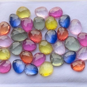 Peut inclure: Une collection de pierres précieuses en vrac, facettées et en forme de poire, dans une variété de couleurs vives, notamment jaune, rose, bleu, orange et gris. Chaque pierre présente une surface polie à facettes multiples qui reflète la lumière.