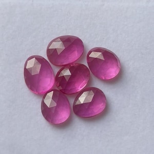 Op de afbeelding: Zes gefacetteerde, ovaalvormige, roze edelstenen liggen op een wit oppervlak. De edelstenen hebben een gepolijst, reflecterend oppervlak en een levendige, verzadigde kleur. De edelstenen zijn waarschijnlijk voor het maken of verzamelen van sieraden.