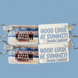 Könnte beinhalten: Zwei Schlüsselanhänger mit einem Teamfoto und dem Text "GOOD LUCK AT SUMMIT! COACH LINDSEY" in Blau. Die Schlüsselanhänger haben silberne Schlüsselringe und einen hellblauen Hintergrund.