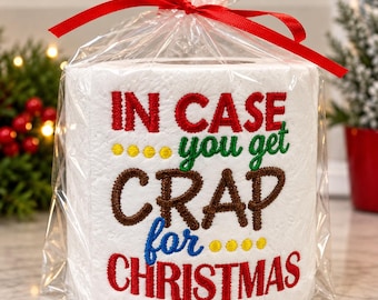 May include: A white toilet paper roll wrapped in clear plastic with a red ribbon bow on top. The roll features embroidered text in red, green, brown, and blue that reads: IN CASE you get CRAP for CHRISTMAS, accented with yellow dots.