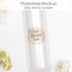 May include: White 20oz skinny tumbler mockup with a gold glitter design that says "Your Design Here". The tumbler is on a white surface with white flowers.
