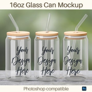 May include: Three clear glass can mockups with bamboo lids and clear straws. Each can has the words "Your Design Here" in black script. The image is labeled "16oz Glass Can Mockup" and "Photoshop compatible".