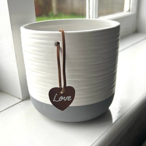 May include: White ceramic planter with a grey base and a brown leather heart-shaped tag that says "Love".