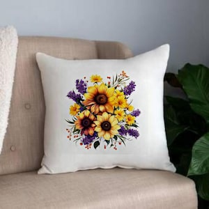 May include: White throw pillow with a floral design featuring sunflowers and purple flowers. The sunflowers are yellow with brown centers and the purple flowers are a light lavender color.