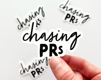 May include: White stickers with the phrase "chasing PRs" in black script and bold block letters. Several stickers are visible, with one held by a hand. The stickers are designed for fitness enthusiasts and those focused on personal records.