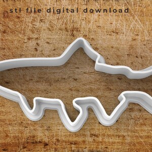 May include: A white plastic 3D printed fish cookie cutter. The cutter is designed with a detailed outline of a fish with fins and a tail.