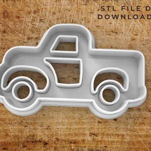 May include: A white plastic 3D printed cookie cutter in the shape of a vintage pickup truck.  The cookie cutter has a rounded cab, a flatbed, and two wheels on each side.  The cookie cutter is designed for use with fondant, cookie dough, or other edible materials.