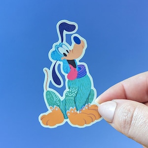 May include: A blue and green cartoon dog wearing a blue and green sweater with a pink collar. The dog is sitting on its hind legs with its front paws raised.