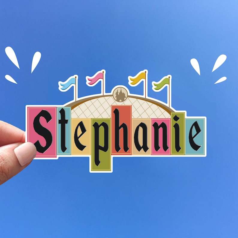 Pode incluir: Um adesivo colorido com o nome "Stephanie" escrito em letras pretas. O adesivo &eacute; projetado para parecer um castelo com bandeiras e uma c&uacute;pula.