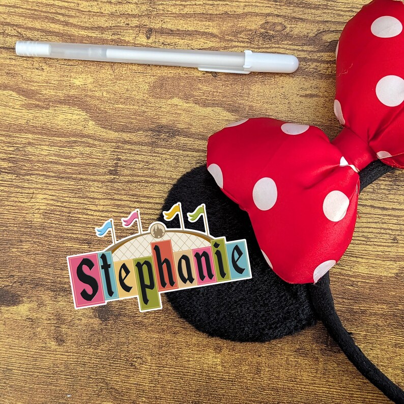 Pode incluir: Uma faixa de cabe&ccedil;a Minnie Mouse de bolinhas vermelhas e brancas com uma orelha preta e um adesivo colorido que diz "Stephanie".