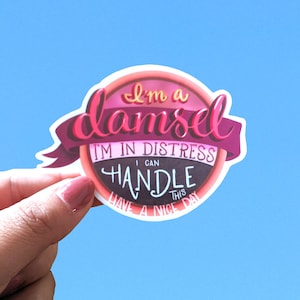 May include: A pink and purple sticker with the text "I'm a damsel I'm in distress I can handle this Have a nice day"