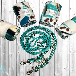 May include: Four turquoise and white fleece horse wraps and a turquoise and white braided leather horse reins with silver hardware. The wraps and reins are rolled up and arranged on a white wood background. The text "Angel's Tack" is visible on the wraps.