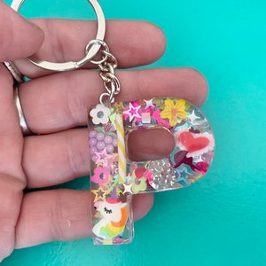 May include: A clear resin keychain shaped like the letter "P" with a unicorn, candy canes, flowers, and glitter inside.