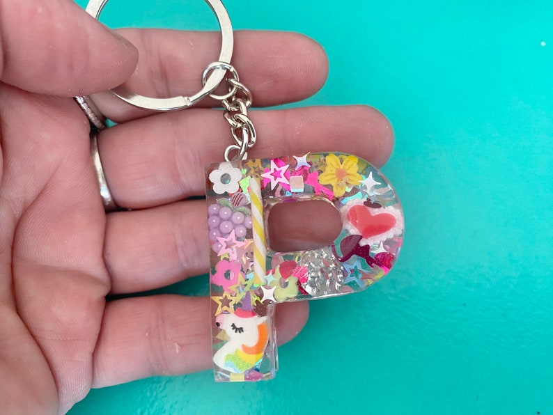 May include: A clear resin keychain shaped like the letter "P" with a unicorn, candy canes, flowers, and glitter inside.