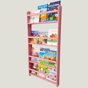 May include: A pink wooden bookshelf with five shelves, filled with colourful children's books. The books have titles in Turkish, including "Yapıştırma Etiketleri" and "Kelebek".