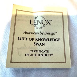 May include: A square, cream-colored Lenox American by Design certificate of authenticity featuring a thin brown border. The text reads Lenox, American by Design, Gift of Knowledge Swan, and Certificate of Authenticity in black lettering.