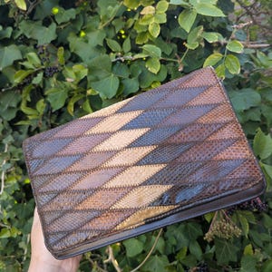 May include: A rectangular clutch bag featuring a geometric diamond pattern constructed from textured, scale-like panels in shades of dark brown, tan, and black. The exterior surface displays a repeating mosaic design with visible stitching.