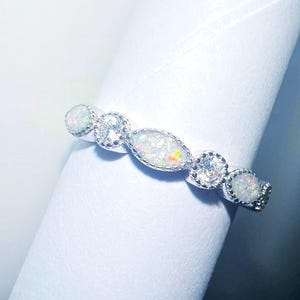 May include: A silver band ring with five white opal stones set in a bezel setting. The stones are oval shaped and have a sparkly finish.