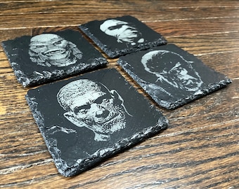 May include: Four black slate coasters with a white etched design of classic horror movie monsters. The coasters feature the Creature from the Black Lagoon, the Wolfman, the Mummy, and Frankenstein's Monster.