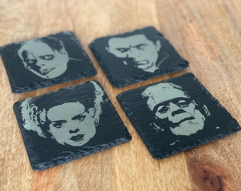 May include: Set of four black slate coasters featuring classic horror movie characters. Each coaster has a different character: Frankenstein, Dracula, The Bride of Frankenstein, and The Phantom of the Opera.