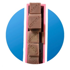 May include: A pink silicone mould filled with six brown bars of soap. Each bar is stamped with the word "ADZUKI" in white.
