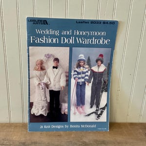 May include: A Leisure Arts craft leaflet titled Wedding and Honeymoon Fashion Doll Wardrobe, Leaflet 2033. The cover features two photographs of dolls in knit outfits: a wedding couple and a pair in winter ski gear. It includes 21 knit designs.