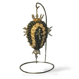 May include: A black and gold beaded Christmas ornament with a decorative stand. The ornament is shaped like a heart and has a beaded fringe.