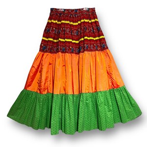 May include: A multi-layered skirt with a red, yellow, and blue patterned top layer, an orange middle layer, and a green bottom layer with white polka dots.
