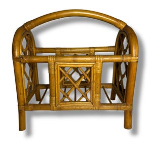 May include: A vintage bamboo magazine rack with a curved handle. The rack features a rectangular frame with a lattice design on the front and sides. The bamboo is a warm, golden-brown color, and the rack has a sturdy, upright design.