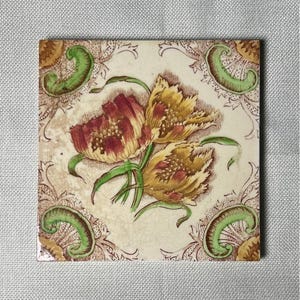 May include: Square ceramic tile featuring a floral design with red and yellow tulips and green leaves. The tile has a cream-colored background with a decorative border in brown and green. The tile is approximately 6 inches by 6 inches.