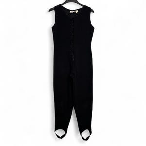 May include: A black sleeveless jumpsuit with a full-length zipper down the front. The jumpsuit has stirrups at the ankles and is hanging on a black hanger. The garment appears to be made of a knitted material.