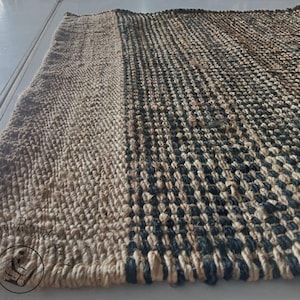 May include: A natural fiber rug with a woven pattern of black and beige. The rug has a textured surface and a simple design.
