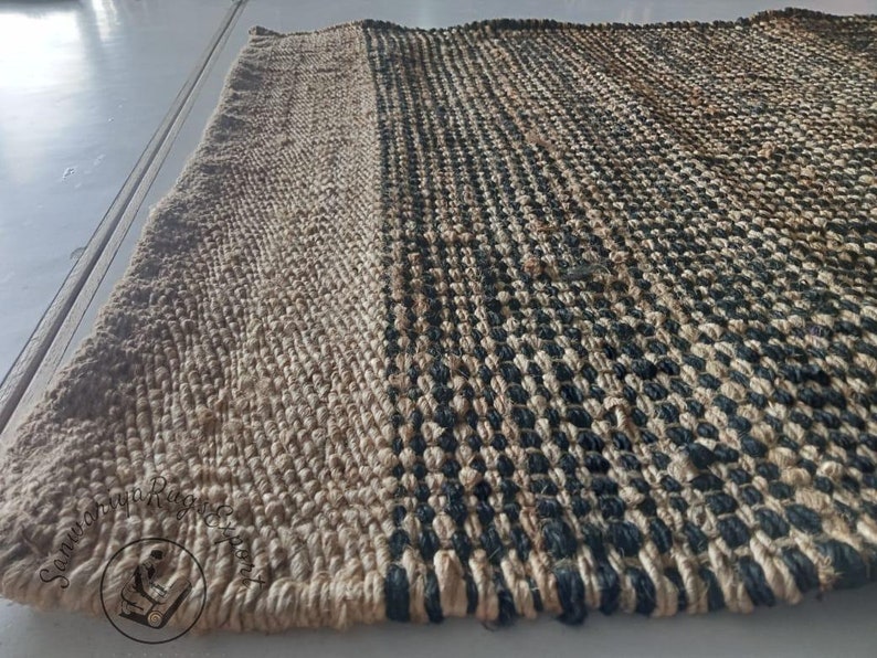 May include: A natural fiber rug with a woven pattern of black and beige. The rug has a textured surface and a simple design.