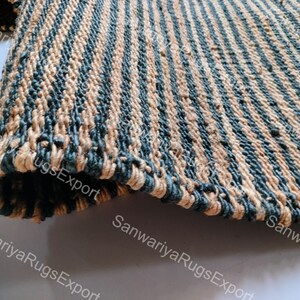 May include: A close-up of a woven rug with alternating stripes of tan and dark blue. The rug is made of natural fibres and has a rough texture.
